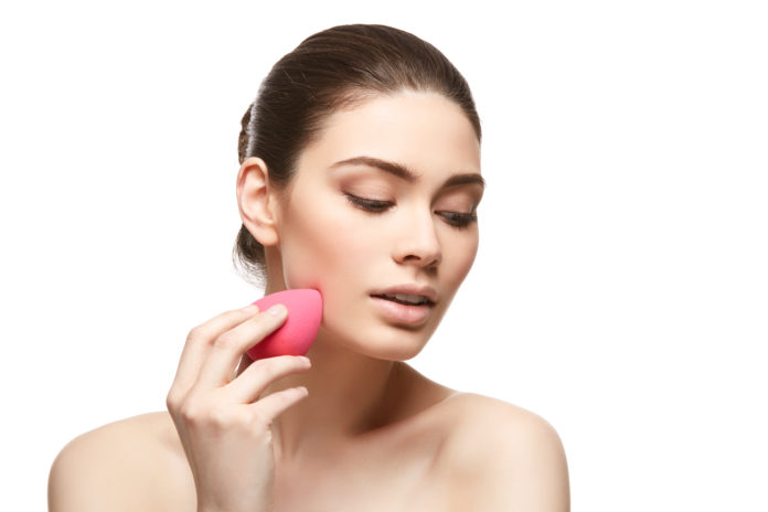 Kobieta używająca różowej gąbeczki do makijażu