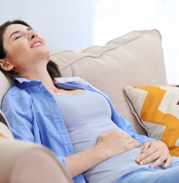 Jak radzić sobie ze wzdęciami? Kobieta ubrana na niebiesko cierpiąca z powodu wzdęć brzucha