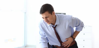 Siedzący tryb życia a problemy ze wzdęciami młody mężczyzna z bólem brzucha stojący przy biurku