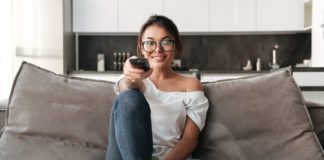 Ulepsz swój telewizor – czyli co nowego w świecie przystawek TV? młoda dziewczyna z pilotem na kanapie