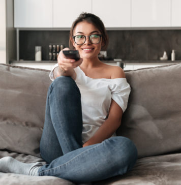 Ulepsz swój telewizor – czyli co nowego w świecie przystawek TV? młoda dziewczyna z pilotem na kanapie