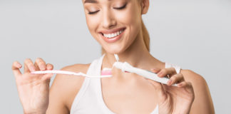 Wybielające pasty do zębów – ścierne, enzymatyczne, a może z nadtlenkiem? kobieta nakładająca pastę do zębów na szczoteczkę