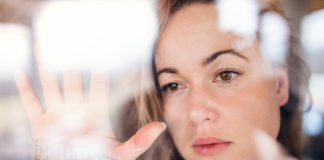 Czym jest syndrom sztokholmski? W jaki sposób się objawia? młoda smutna kobieta za szybą