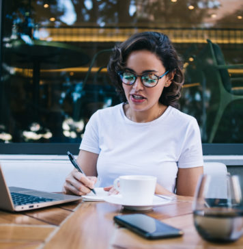 Planery, motywatory – skąd moda na tego typu publikacje? kobieta w kawiarni robiąca notatki w planerze